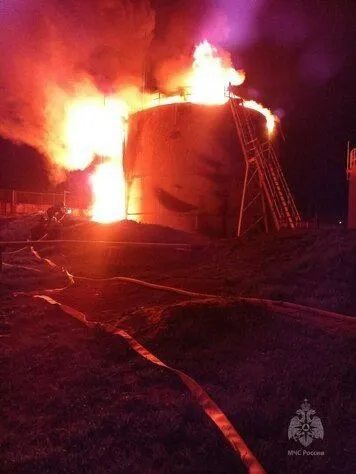 Réservoir de dépôt pétrolier en flammes la nuit, lances à incendie au sol
