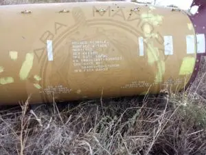 Débris d’un corps de missile jaune couvert d’inscriptions, tombé dans un champ