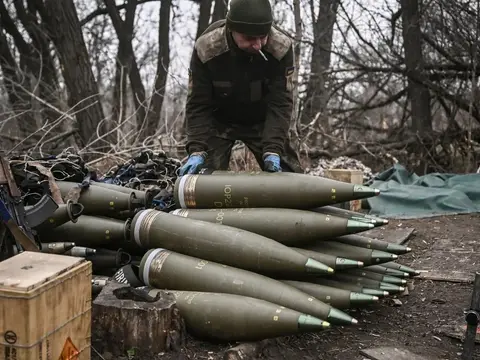 Un soldat ukrainien range des obus d’artillerie alignés au sol dans un bois d’hiver