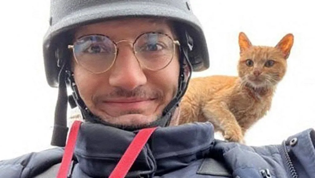 Journaliste casqué en gilet pare-balles, un chat roux perché sur son épaule