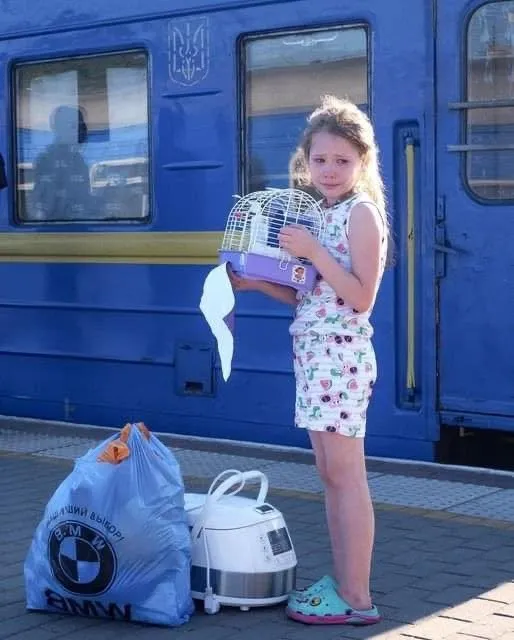 Fillette en larmes serrant une cage à oiseau devant un train ukrainien
